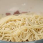 Cooked spaghetti rests over bacon in a pan before the carbonara sauce is added