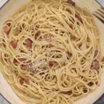 Spaghetti carbonara with bacon, grated cheese and black pepper in a light blue pot