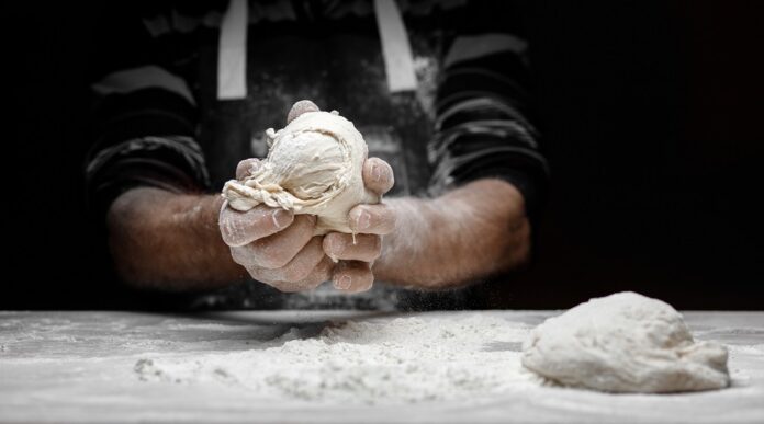 pastry chef claps hands and prepares yeast dough for pizza pasta