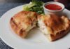 Golden-brown Italian panzerotti cut open to reveal melted cheese and ham, served with marinara dipping sauce and fresh lettuce on a white plate