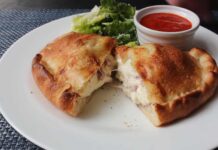 Authentic Italian Panzerotti with Ham and Cheese Recipe Golden-brown Italian panzerotti cut open to reveal melted cheese and ham, served with marinara dipping sauce and fresh lettuce on a white plate
