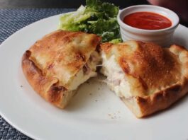 Golden-brown Italian panzerotti cut open to reveal melted cheese and ham, served with marinara dipping sauce and fresh lettuce on a white plate