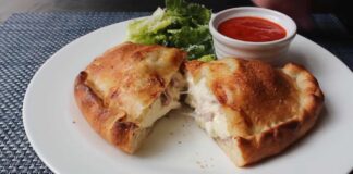 Golden-brown Italian panzerotti cut open to reveal melted cheese and ham, served with marinara dipping sauce and fresh lettuce on a white plate