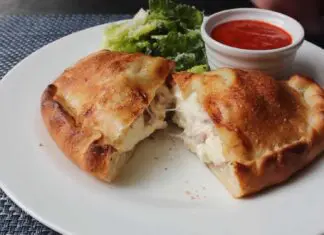 Golden-brown Italian panzerotti cut open to reveal melted cheese and ham, served with marinara dipping sauce and fresh lettuce on a white plate