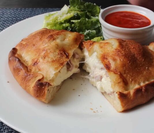 Golden-brown Italian panzerotti cut open to reveal melted cheese and ham, served with marinara dipping sauce and fresh lettuce on a white plate