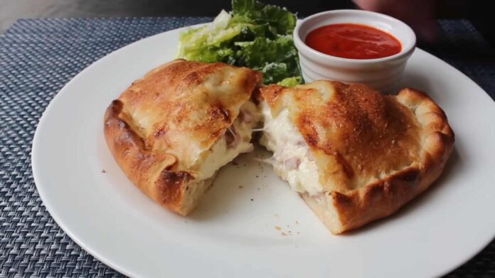 Authentic Italian Panzerotti with Ham and Cheese Recipe Steps Golden-brown Italian panzerotti cut open to reveal melted cheese and ham, served with marinara dipping sauce and fresh lettuce on a white plate