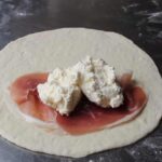 Rolled panzerotti dough topped with ham slices and soft cheese filling on a floured work surface before sealing