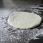 Round ball of homemade panzerotti dough resting on a floured countertop before shaping and filling