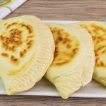 Four homemade Italian panzerotti filled with ham and cheese served on a white plate with golden-brown crusts