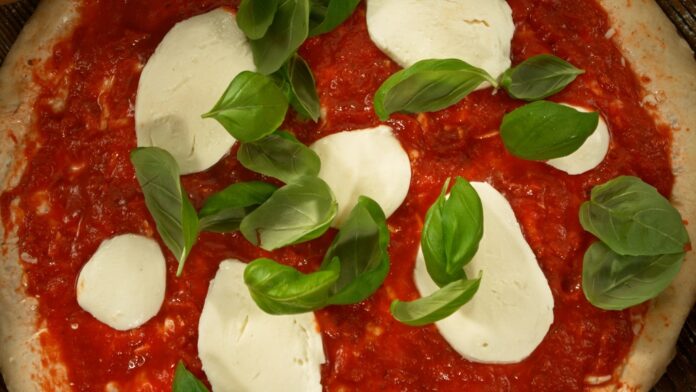 Unbaked Margherita pizza with mozzarella, fresh basil leaves, and tomato sauce on pizza dough
