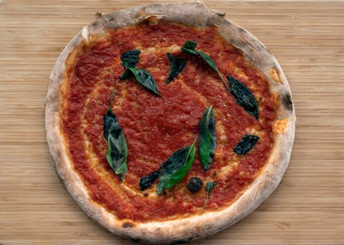 Traditional pizza topped with marinara sauce and fresh basil leaves on a wooden board.