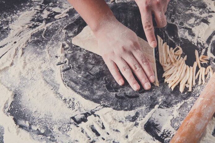 Fresh pasta dough being rolled and cut by hand on a floured work surface, demonstrating homemade wheat flour pasta preparation