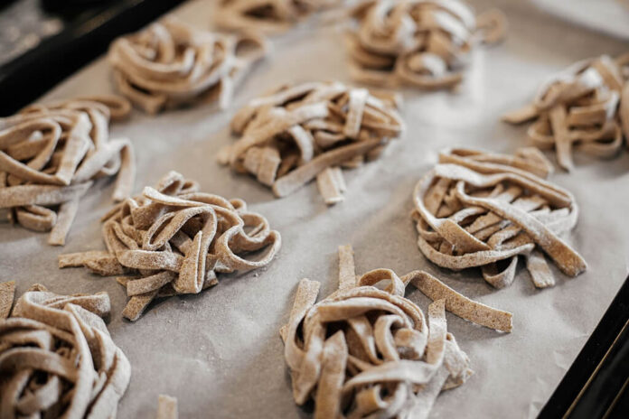 Fresh whole wheat pasta nests resting on parchment paper, showing the darker color and rustic texture of whole wheat dough