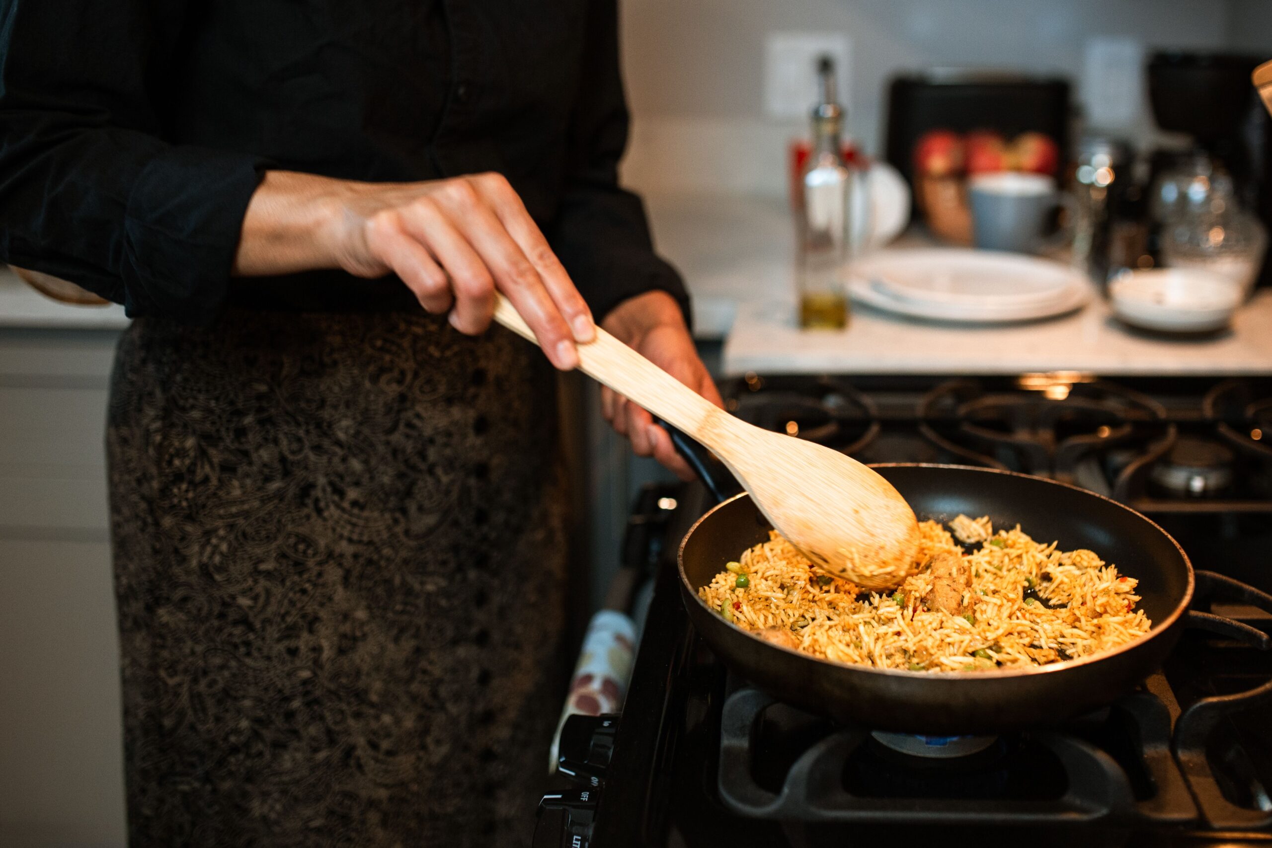 Cook stirring rice in a frying pan on a gas stove, illustrating the wide cooking surface used for risotto.