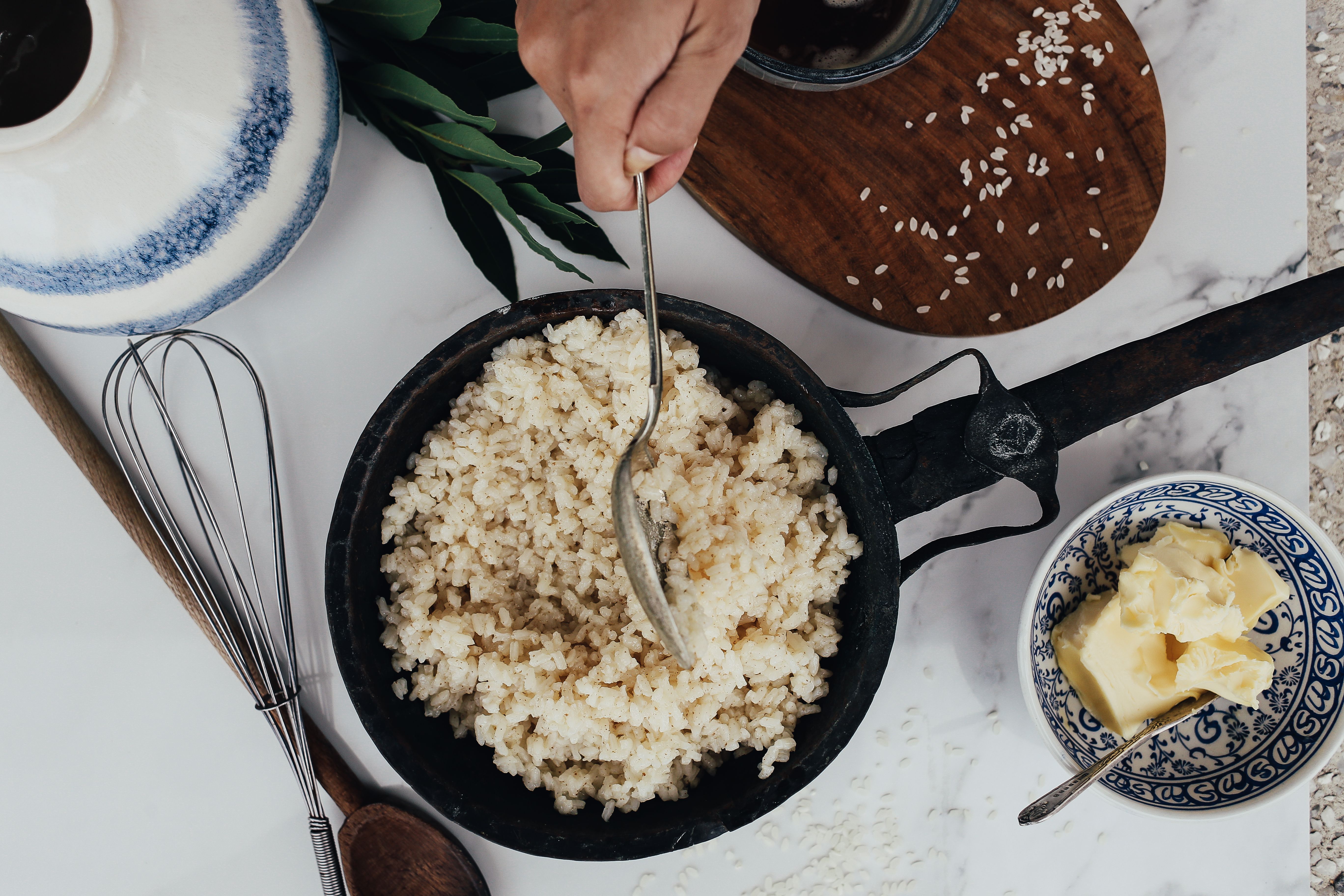 Overhead view of rice cooking in a frying pan with butter and utensils, highlighting the pan's broad base.